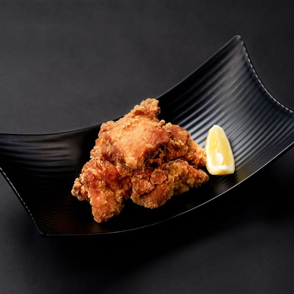 Crispy Japanese fried chicken (karaage) with a lemon wedge on a black wavy plate.