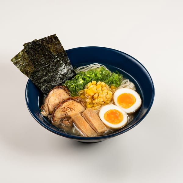Taro ramen bowl with noodles, pork, corn, green onions, bamboo shoots, nori, and soft-boiled eggs.