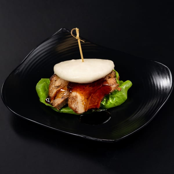 Japanese pork belly bao bun with lettuce and sauce on a black plate.