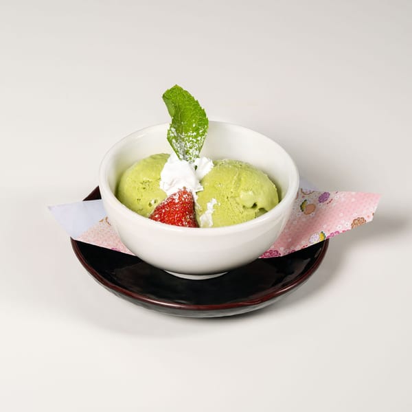 Matcha green tea ice cream with whipped cream, strawberry, and mint in a white bowl.