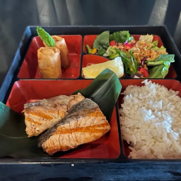 A Taro Japanese bento box with grilled salmon, spring rolls, rice, and a fresh salad.