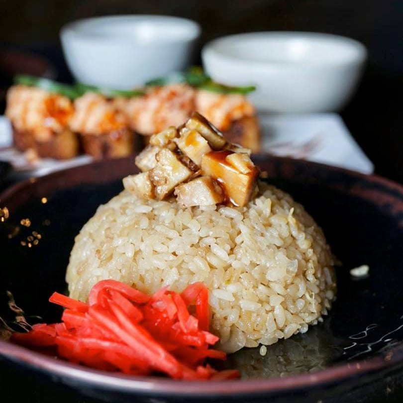 Japanese fried rice with mushrooms and red pickled ginger, with sushi rolls in the background.