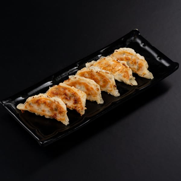 Six pan-fried Japanese gyoza, golden brown and crispy, arranged on a black rectangular plate.