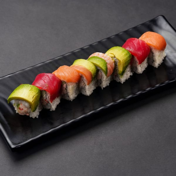 A row of colorful Taro sushi rolls with avocado, tuna, salmon, and shrimp on a black plate.